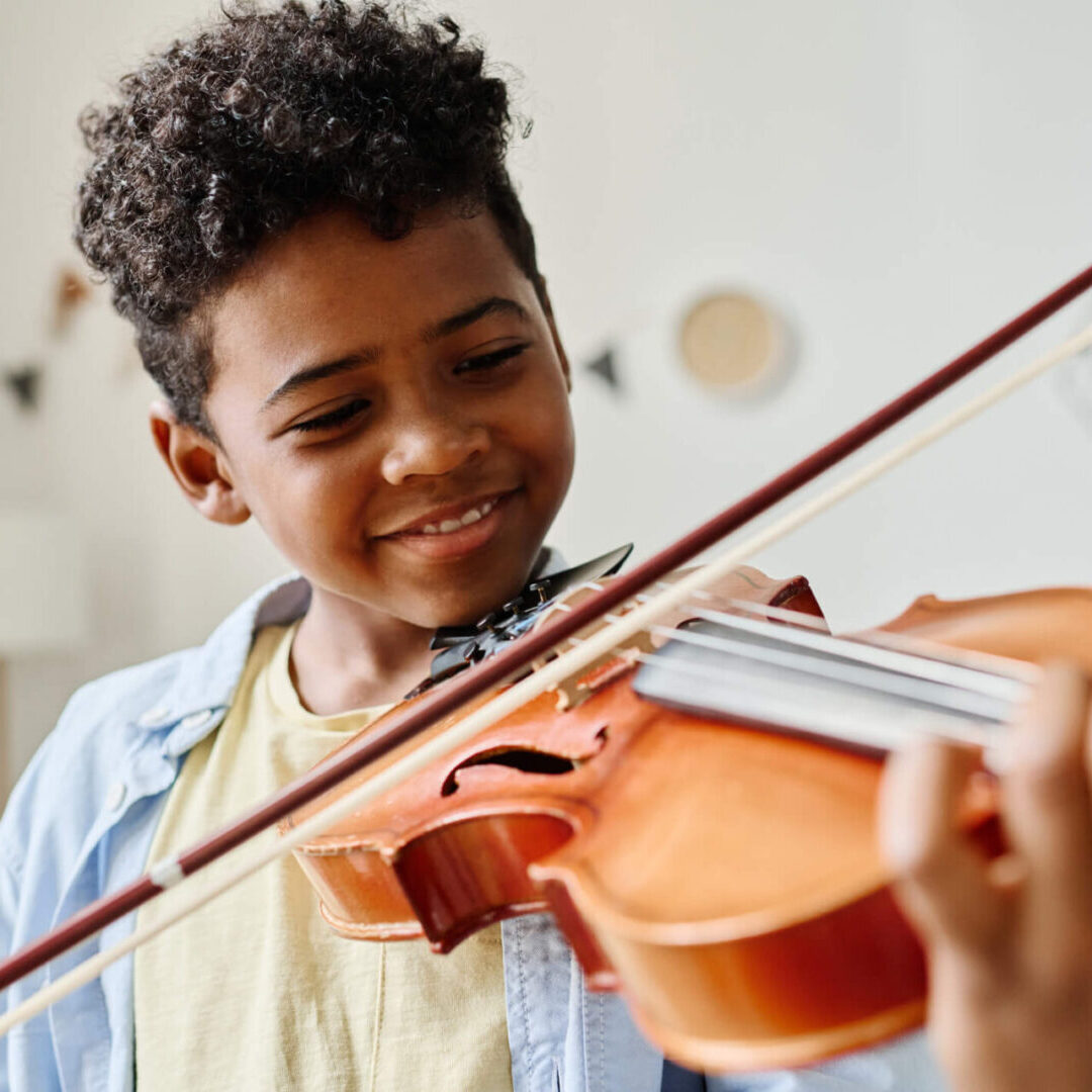 A young boy smiles as he plays the violin. fundraiser